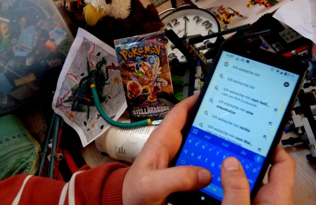 Die Hände eines etwa zehnjährigen Kindes geben die Suchanfrage "Ich wünsche mir..." in ein Smartphone ein. Im Hintergrund ist unordentliches Spielzeug zu sehen., © Felix Engel