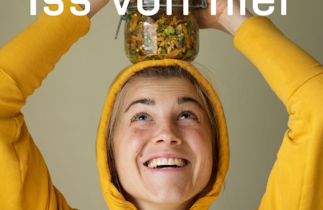 junge Frau im gelben Pullover die ein Glas mit Rohkostsalat auf dem Kopf balanciert und einen Löffel in der Hand hält, © Greenpeace Media