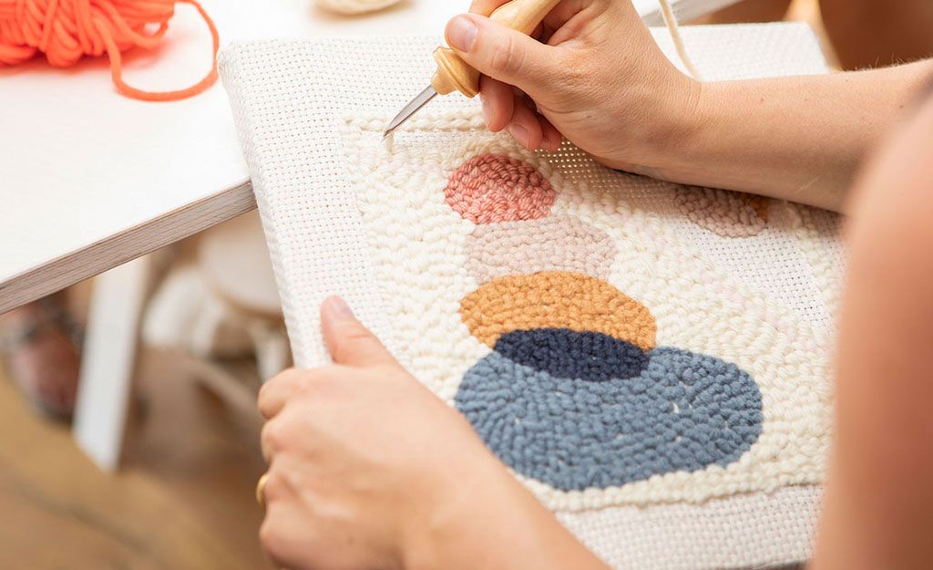 zwei Hände beim Knüpfen eines Wandteppichs mit der Punch-Needle