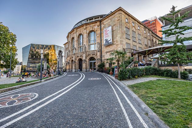 Blick auf das Theater Freiburg. Im Hintergrund ist die Fassade der Universitätsbibliothek Freiburg zu sehen. 