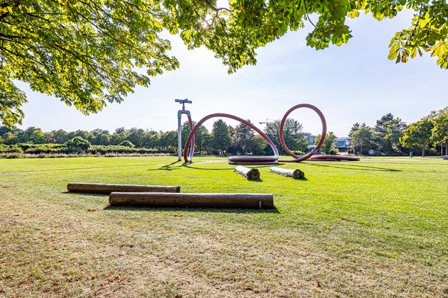 Park mit einem Kunstobjekt in Form eines Gartenschlauchs und Bäumen im Hintergrund 