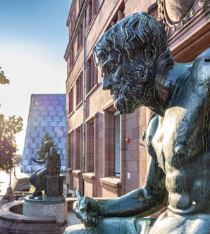 Eingang der Universität Freiburg mit 2 Staturen vor dem Eingang und im Hintergrund die Universitätsbibliothek 