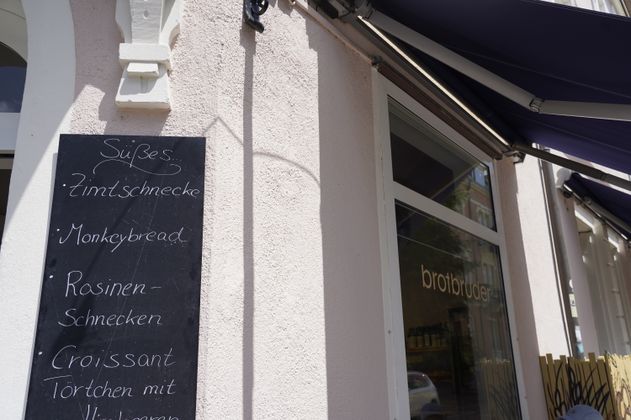 Außenansicht einer Bäckerei mit Tafel, die süße Backwaren anbietet.
