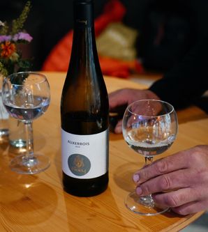 Eine Flasche Auxerrois-Wein auf einem Holztisch mit einem Glas in der Hand einer Person.