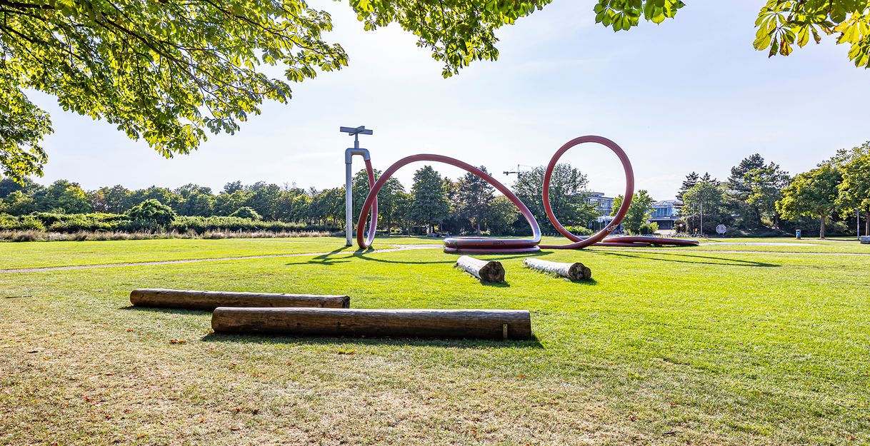 Park mit einem Kunstobjekt in Form eines Gartenschlauchs und Bäumen im Hintergrund 