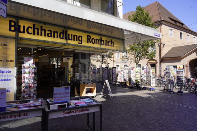Eingang der Buchhandlung Rombach mit Sonderangeboten und Postkartenständern draußen.
