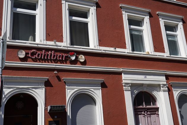 Fassade einer roten Bar mit dem Schriftzug 'Cohibar' und Ganter-Logos.