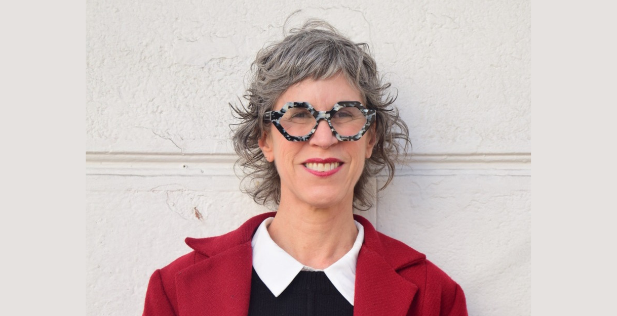 Die Autorin Nona Fernandez steht vor einer grauen Wand. Sie trägt einen roten Mantel und einen schwarzen Pulli.