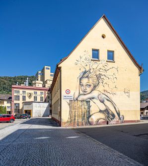 Gebäude der Ganter Brauerei mit Graffiti an der Seite, wo sich eine Gestalt auf einem Baumstumpf abstützt 