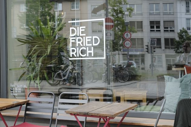 Außenansicht des Co-Workings mit roten Stühlen und Holztischen vor dem Fenster.