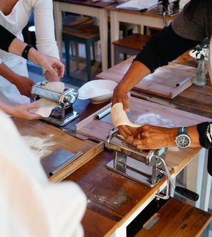 Personen rollen Teig mit Nudelmaschinen auf Holztischen aus.