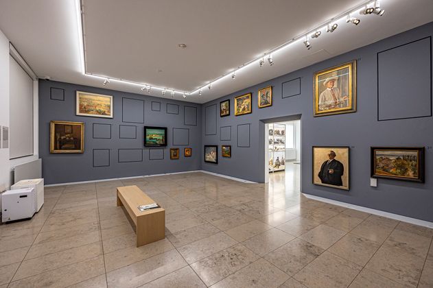 Innenraum mit blauen Wänden an denen verschiedene Bilder hängen iedene B