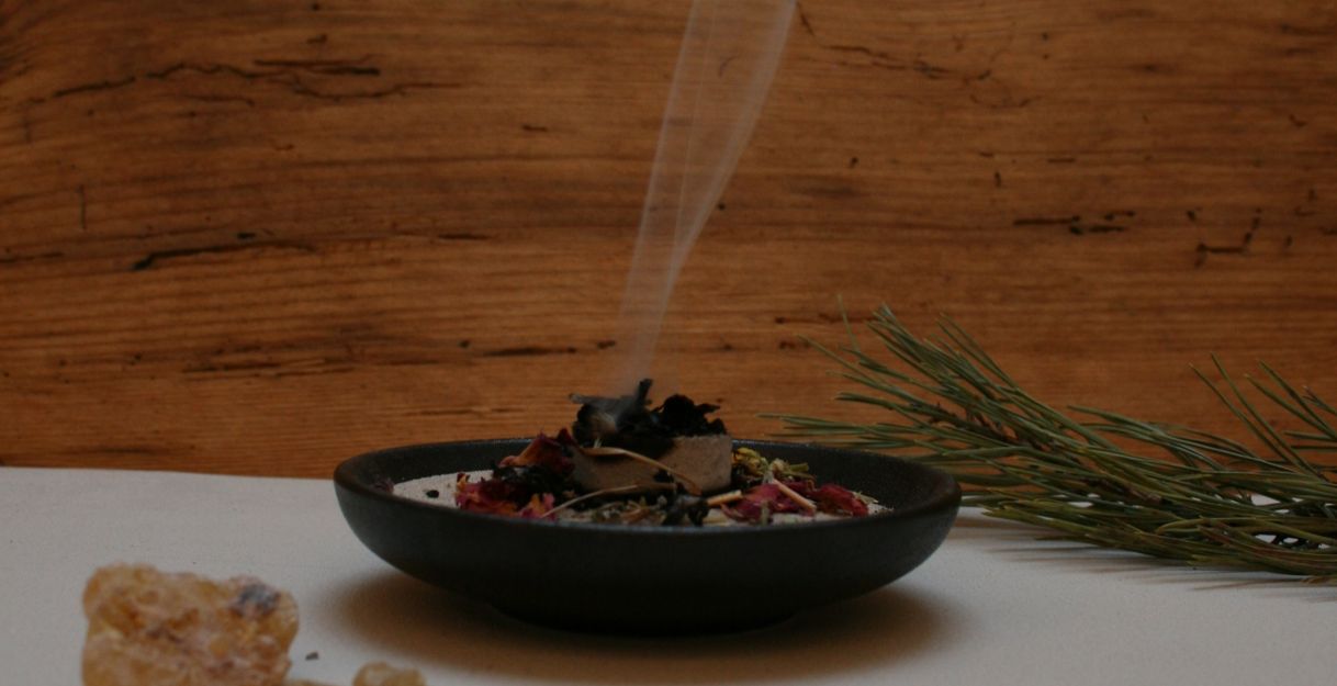 Eine Räucherschale vor einer Holzwand, die Kräuter darauf werden gerade verräuchert.