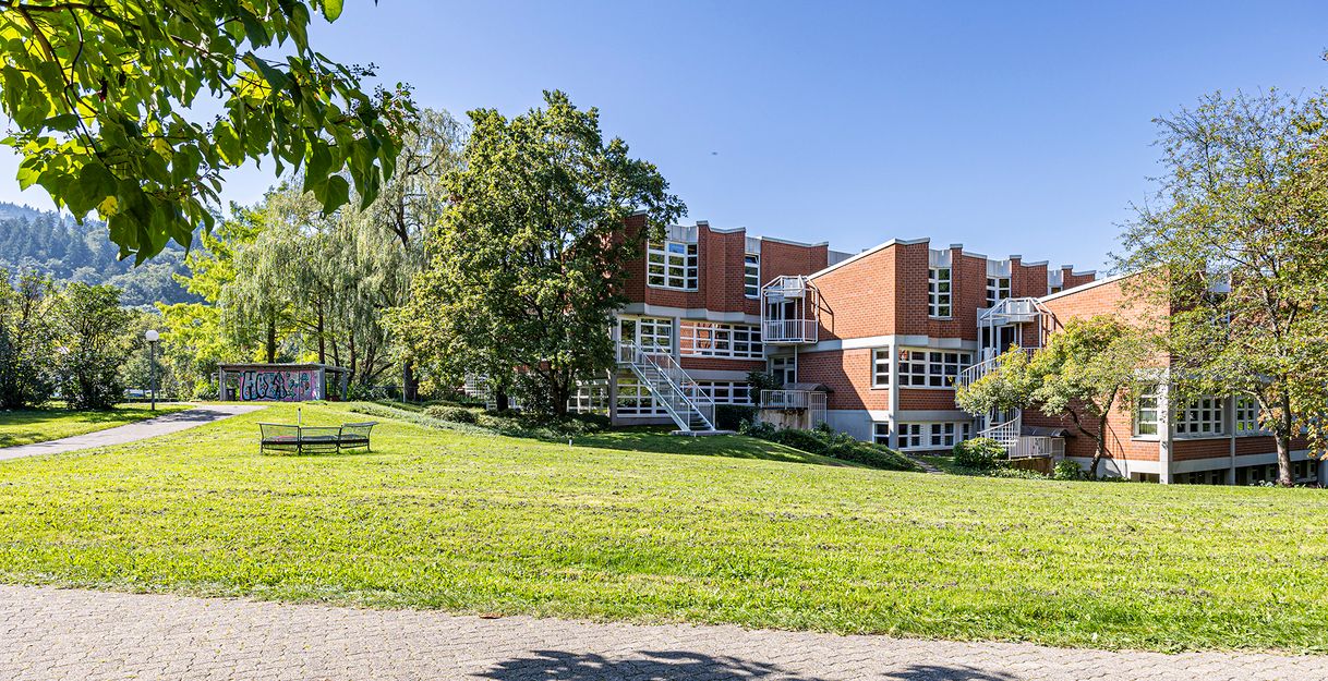 Gebäude mit roter Fassade auf begrüntem Gelände 