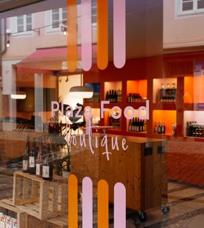 Schaufenster der Plaza Food Boutique mit Flaschen und Regalen im Inneren.